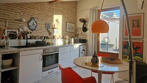 A kitchen with a brick wall, white cabinets, a round table, and red chairs. - Dupleix and an open-air terrace (Saint-Gilles)