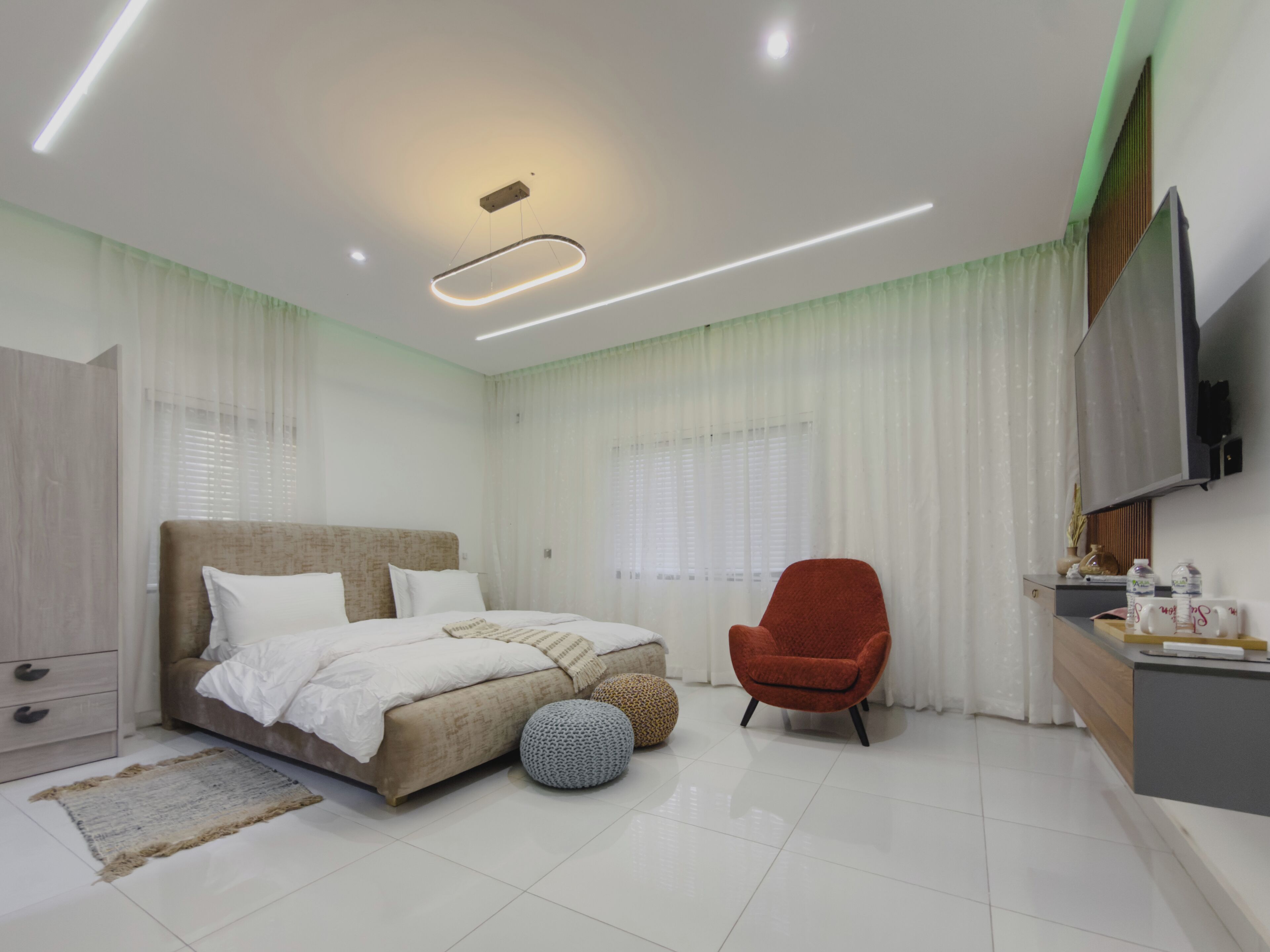 Une chambre moderne avec un lit, un fauteuil rouge, un bureau doté d’un téléviseur à écran plat et une grande fenêtre avec des rideaux.