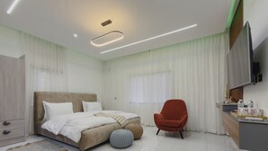 Une chambre moderne avec un lit, un fauteuil rouge, un bureau doté d’un téléviseur à écran plat et une grande fenêtre avec des rideaux.