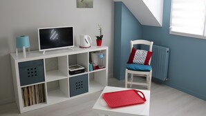 A room with a white TV stand, a red tray, a white chair with a blue cushion, and a radiator.