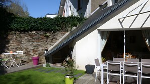 A house with a stone wall, a wooden deck, outdoor furniture, and a potted plant.