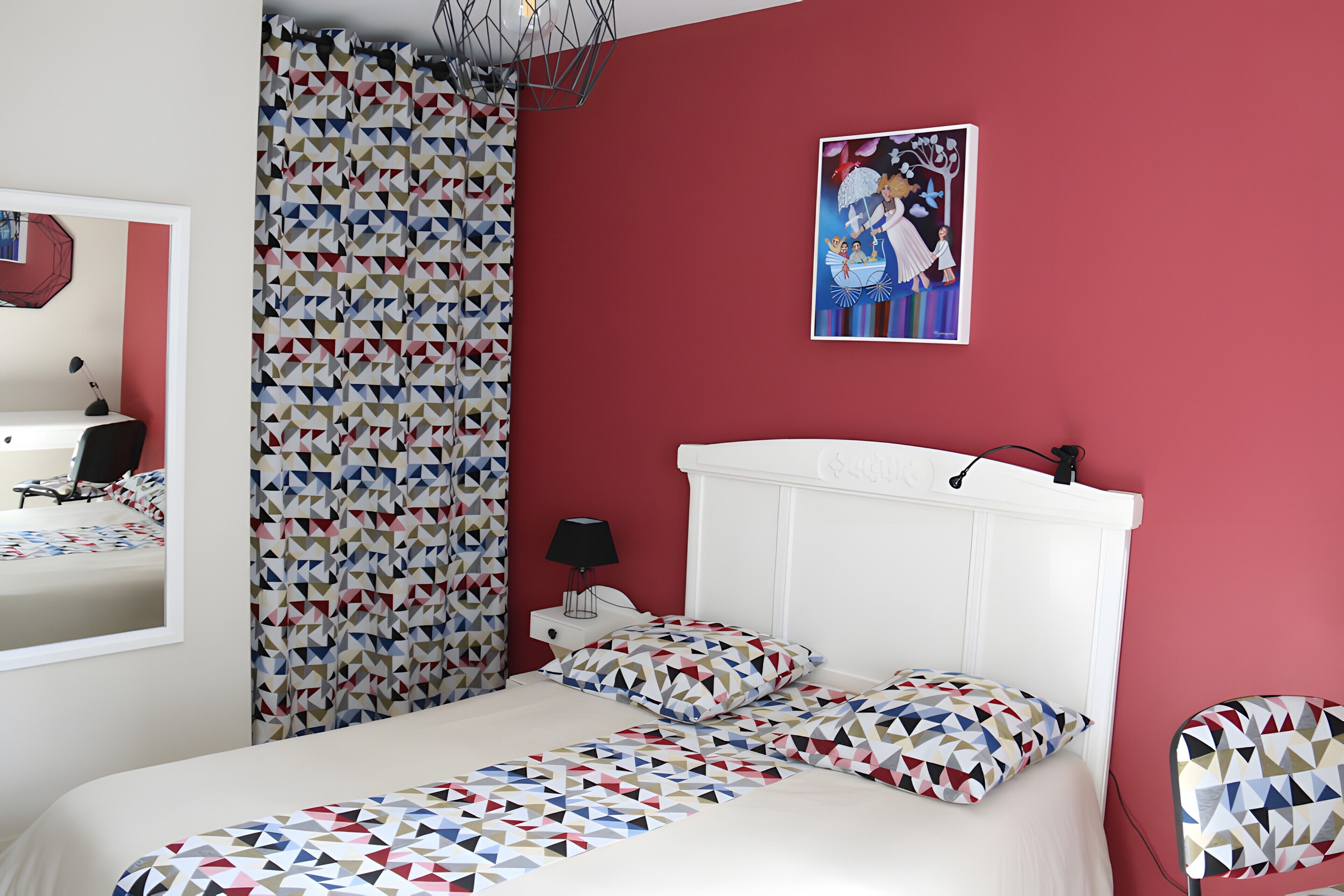 Una cama con una colcha de diseño geométrico, un cabecero blanco y una pared de acento roja.