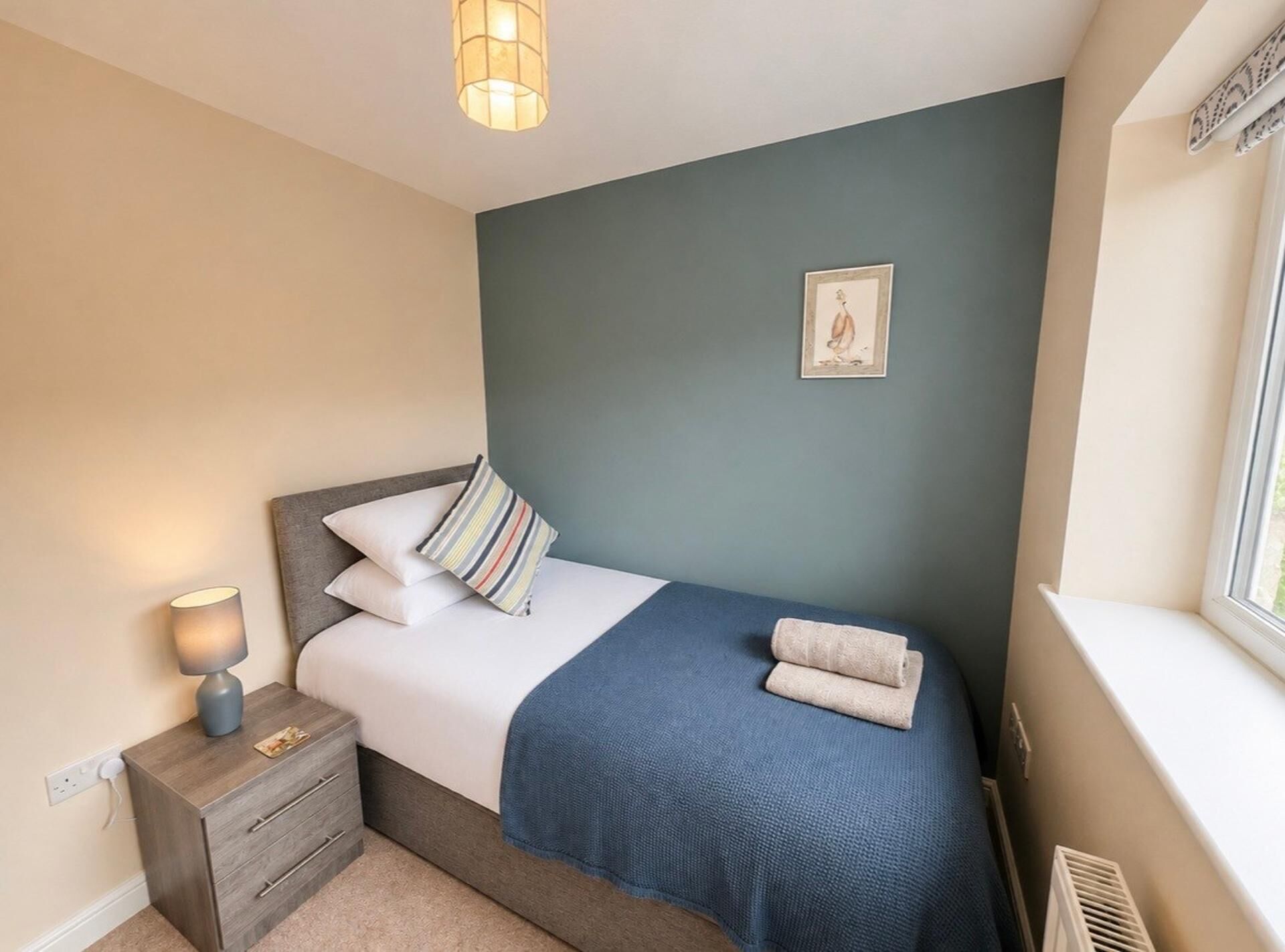 A bedroom with a bed, bedside lamp, nightstand, and a window.