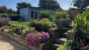 Una casita azul rodeada de un jardín con diversas plantas y flores.