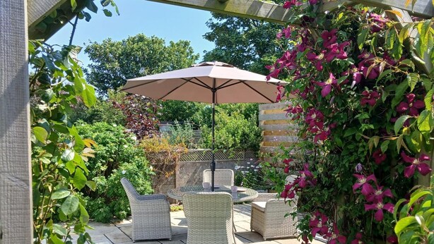 Un patio con mobiliario de mimbre y una pérgola con sombrilla.
