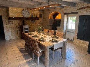Ein Essbereich mit einem Holztisch, gedeckt für sechs Personen, umgeben von Korbstühlen, einer Steinwand und einer Uhr.