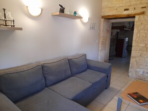 Ein Wohnzimmer mit grauem Sofa, Wandregalen mit Dekoration und einer Tür zu einem anderen Raum.