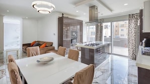 Een moderne keuken met een centraal eiland, een eethoek met een witte tafel en een bank met oranje kussens.