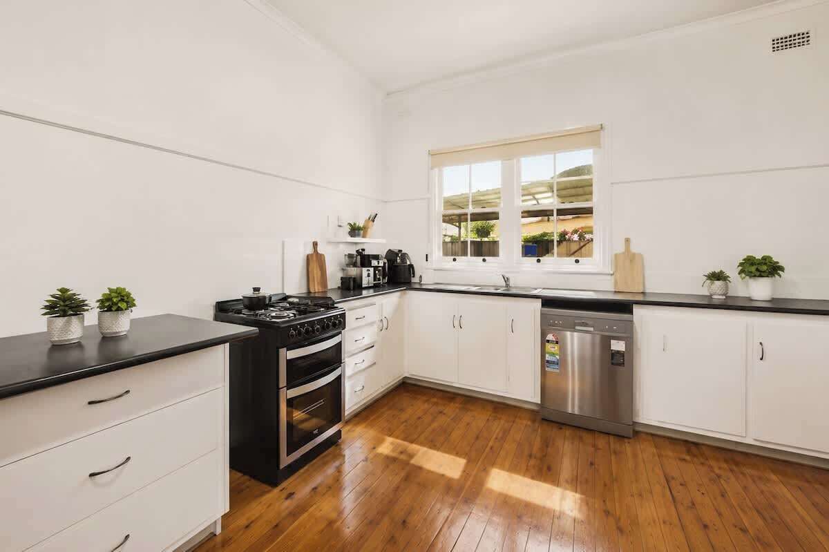 A modern kitchen with white cabinetry, a black countertop, stainless steel appliances, and wooden flooring.