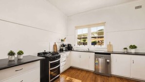 A modern kitchen with white cabinetry, a black countertop, stainless steel appliances, and wooden flooring. - Modern Family house with BBQ (Dubbo)