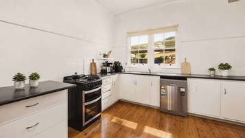 A modern kitchen with white cabinetry, a black countertop, stainless steel appliances, and wooden flooring.