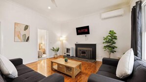 A modern living room with a fireplace, a TV mounted on the wall, and a large plant. - Modern Family house with BBQ (Dubbo)