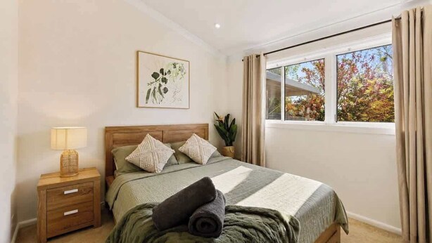 A bedroom with a bed, nightstand, lamp, and window with curtains. - Modern Family house with BBQ (Dubbo)