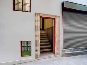 A building entrance with a wooden door, a staircase leading inside, and a closed garage door. - Deluxe Hotel O Dashashwamedh Ghat (Varanasi)