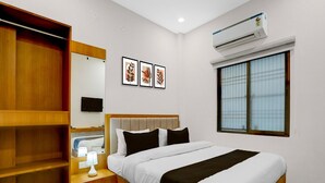 Hotelkamer met een bed, een kledingkast, een nachtkastje met lamp, een aan de muur bevestigde televisie, kunstwerken in lijsten, een airconditioning en een raam met jaloezieën.