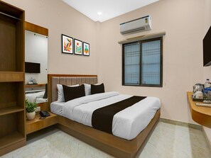 A hotel room with a bed, a bedside table, a mirror, a window, and an air conditioning unit. - Deluxe Hotel O Dashashwamedh Ghat (Varanasi)