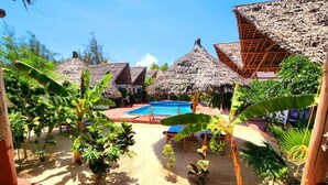 Un espace piscine agrémenté de structures à toits de chaume, entouré de plantes tropicales.