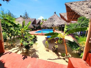 A pool area with thatched-roof structures, surrounded by tropical plants. - Mkeka Spice Lodge Jambian (Unguja South Region)