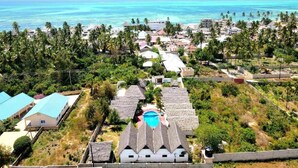 Un village côtier avec des maisons aux toits de chaume, une piscine et une vue sur l’océan.