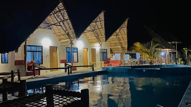 Un complexe hôtelier doté de bâtiments à toits de chaume, d’une piscine et d’un espace de détente en plein air.