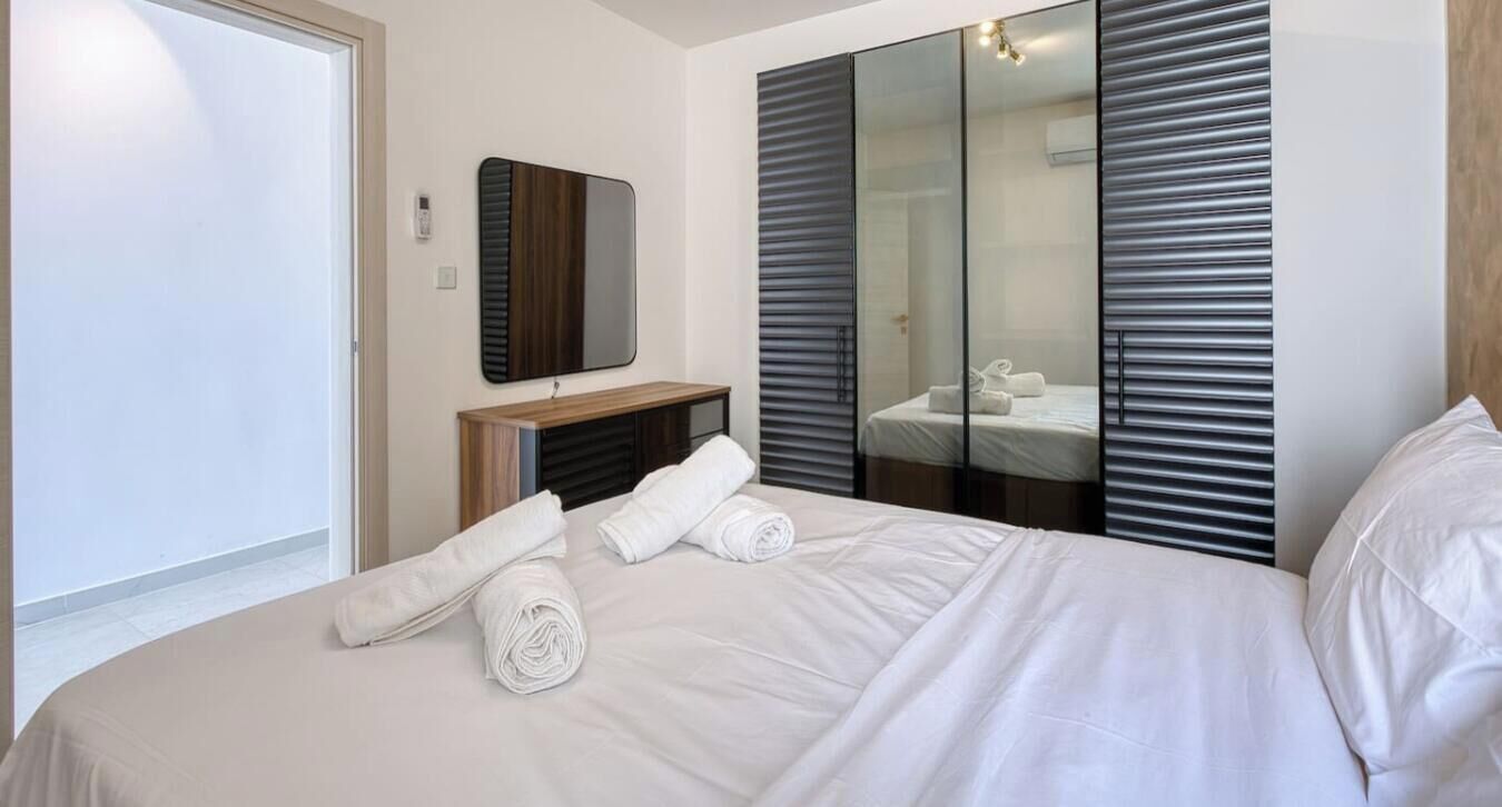 A hotel room with a bed, a mirror, a wardrobe, and a bathroom visible through a glass door.
