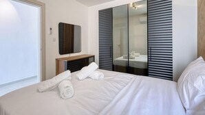 Habitación de hotel con cama, espejo, armario y baño visible a través de una puerta de cristal.