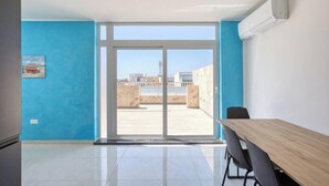 Una habitación con un gran ventanal corredero que da a una terraza exterior, una mesa de madera y una silla.