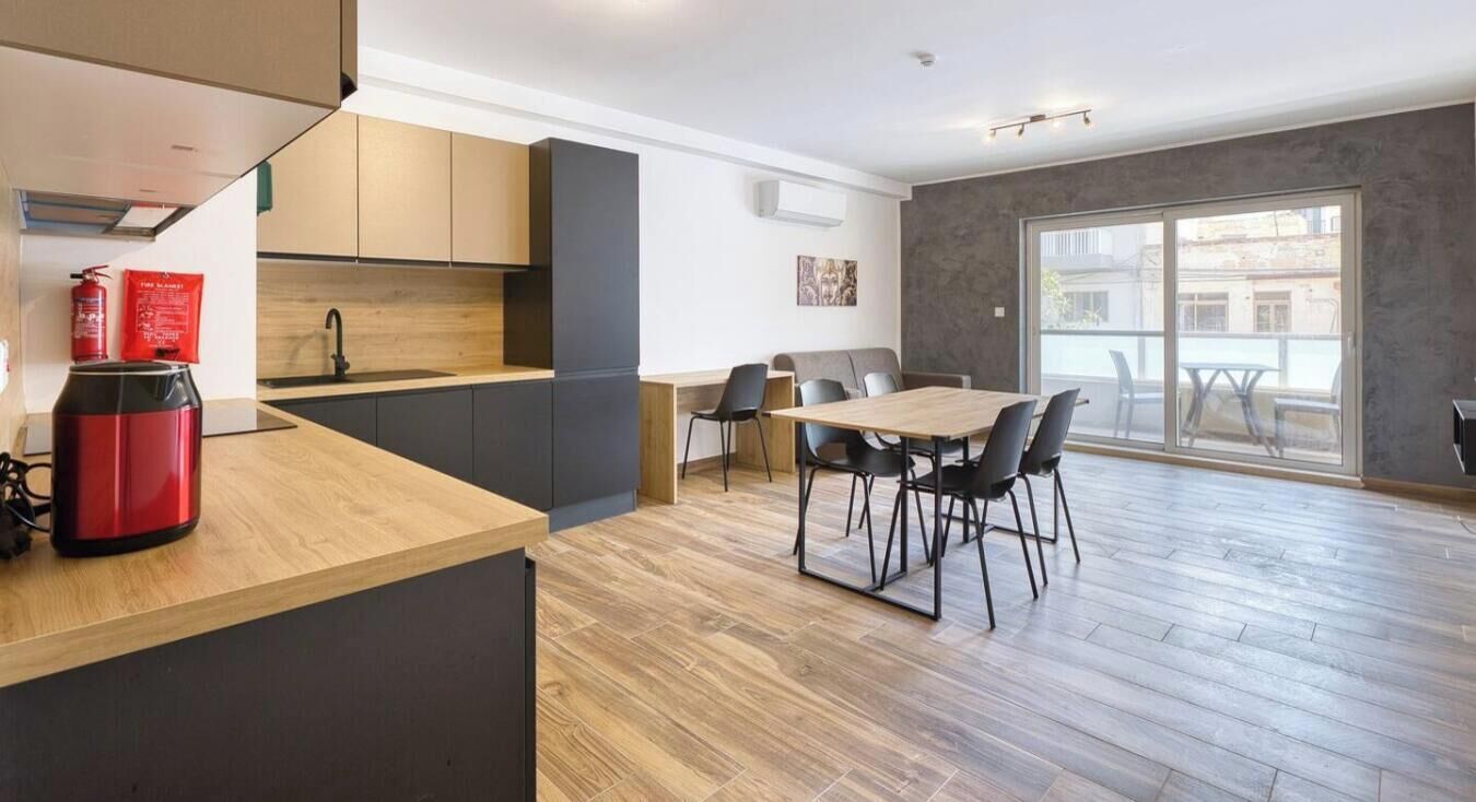 A modern kitchen with a wooden countertop, a dining area with a table and chairs, and a large sliding glass door leading to an outdoor balcony.