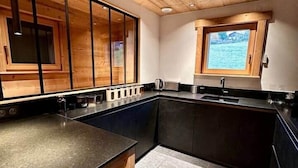 A modern kitchen with wooden cabinets, a black countertop, and a window with a view. - Ma Biche: a beautiful chalet with a lake view and a Nordic hot tub! (Gérardmer)