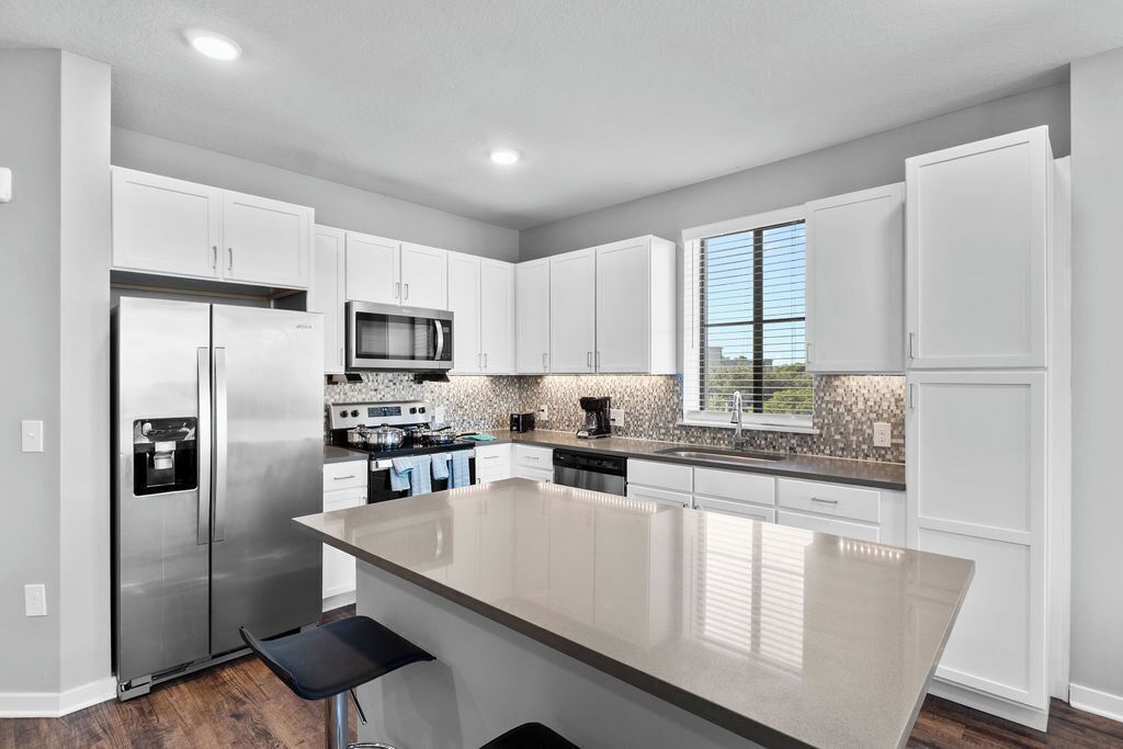 A modern kitchen with white cabinetry, stainless steel appliances, and a large island.