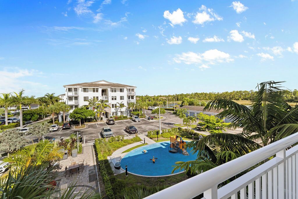 A residential building with a swimming pool, surrounded by greenery and parked cars.