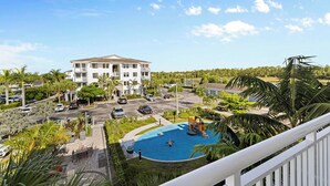 Un edificio residencial con piscina, rodeado de vegetación y automóviles estacionados.