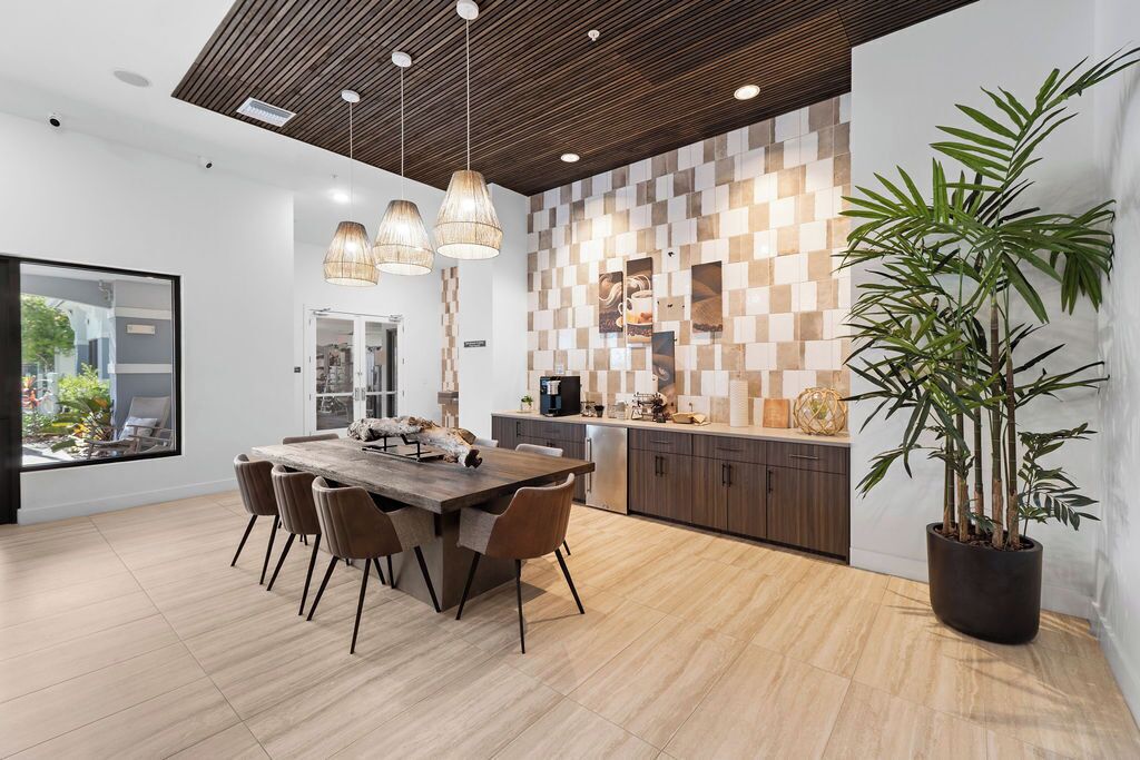 A modern kitchen with a wooden dining table, chairs, and pendant lights.