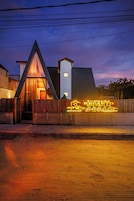 Um edifício moderno com uma entrada triangular destacada, um letreiro de neon e um caminho de acesso pavimentado.