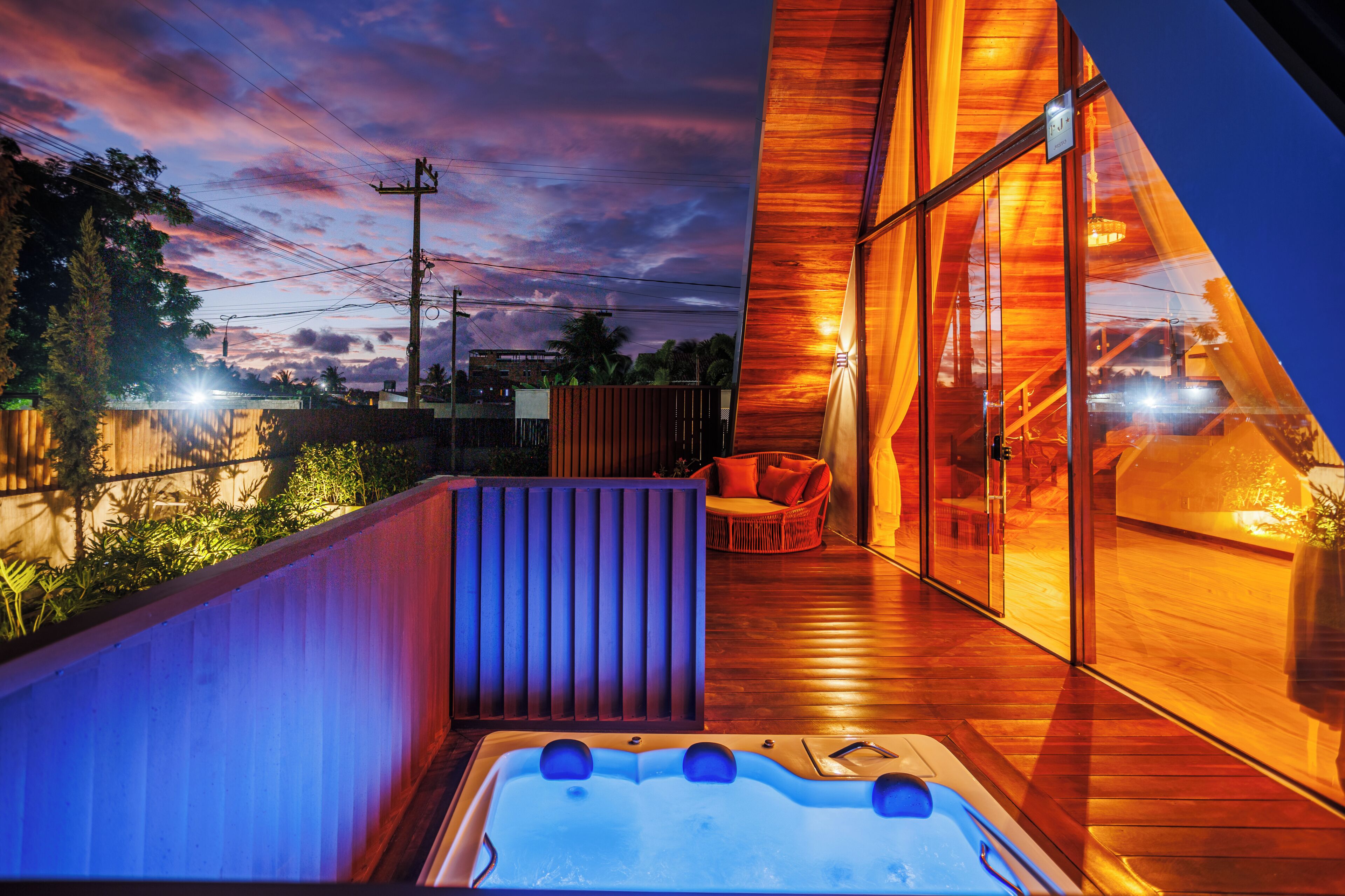 Un espace extérieur moderne doté d’un jacuzzi, d’une terrasse en bois et de murs en verre offrant une vue sur le ciel et les environs.