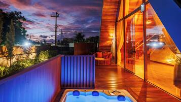 Un espace extérieur moderne doté d’un jacuzzi, d’une terrasse en bois et de murs en verre offrant une vue sur le ciel et les environs.