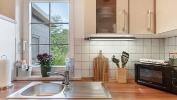 Una cocina con un lavamanos de acero inoxidable, encimera de madera, un microondas y una ventana con vista a la vegetación.
