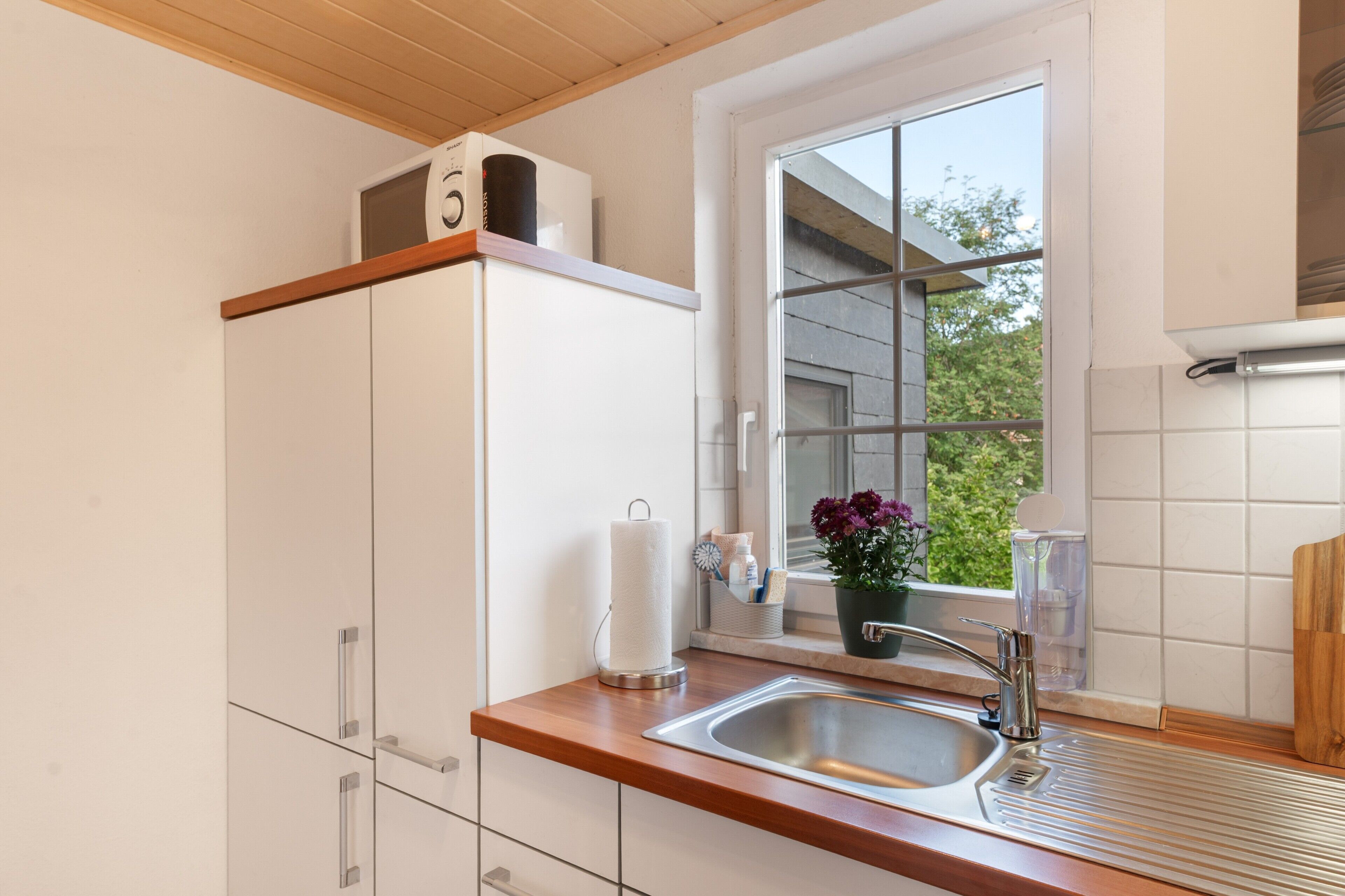 A kitchen with a wooden countertop, a stainless steel sink, a window with a view of greenery, and a white cabinet with a number '5' on top.