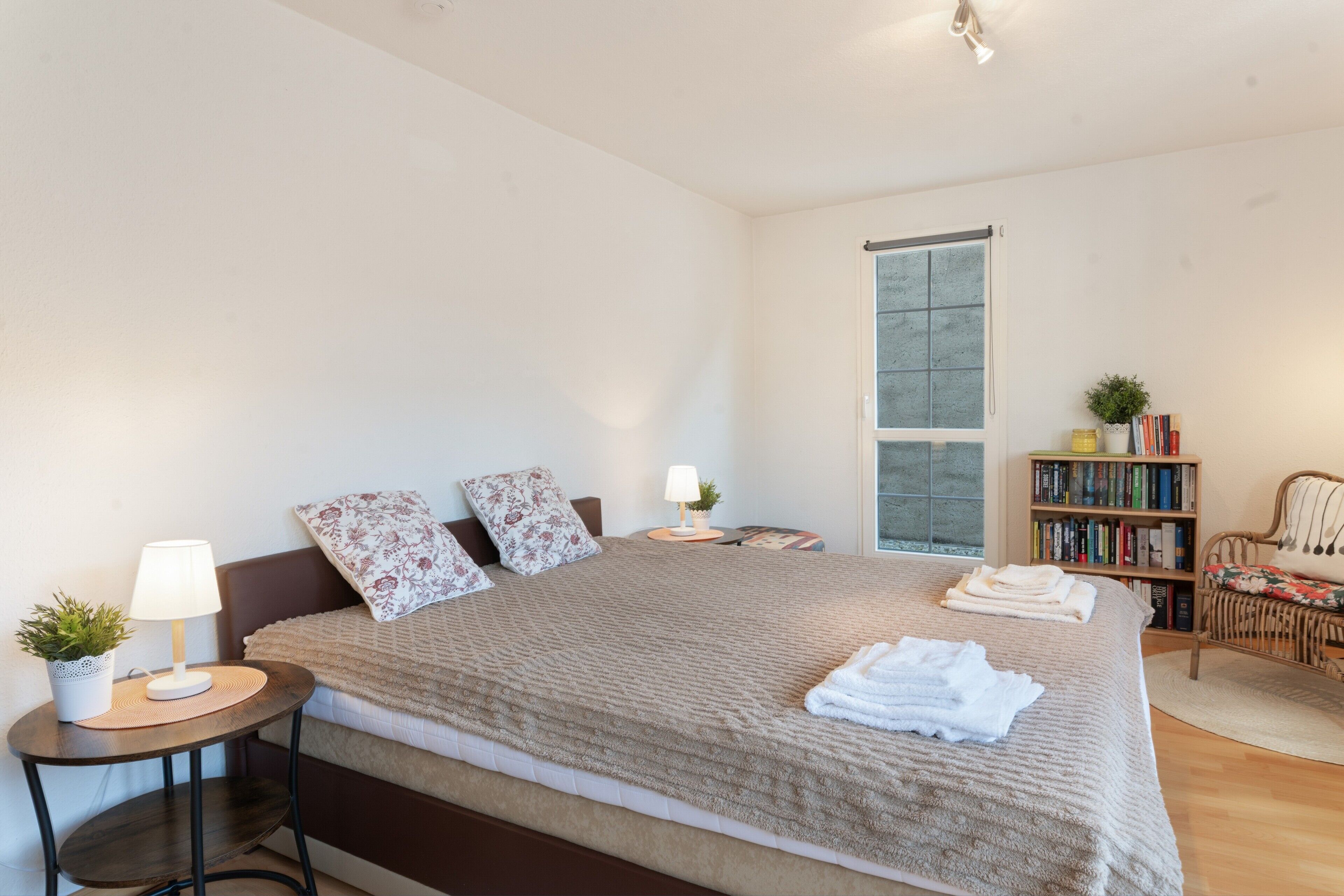 Una camera da letto con un letto, comodini, una lampada, una libreria e una finestra.