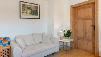 Una habitación con un sofá color beige, una mesita redonda con una lámpara, una puerta de madera y un cuadro enmarcado en la pared.