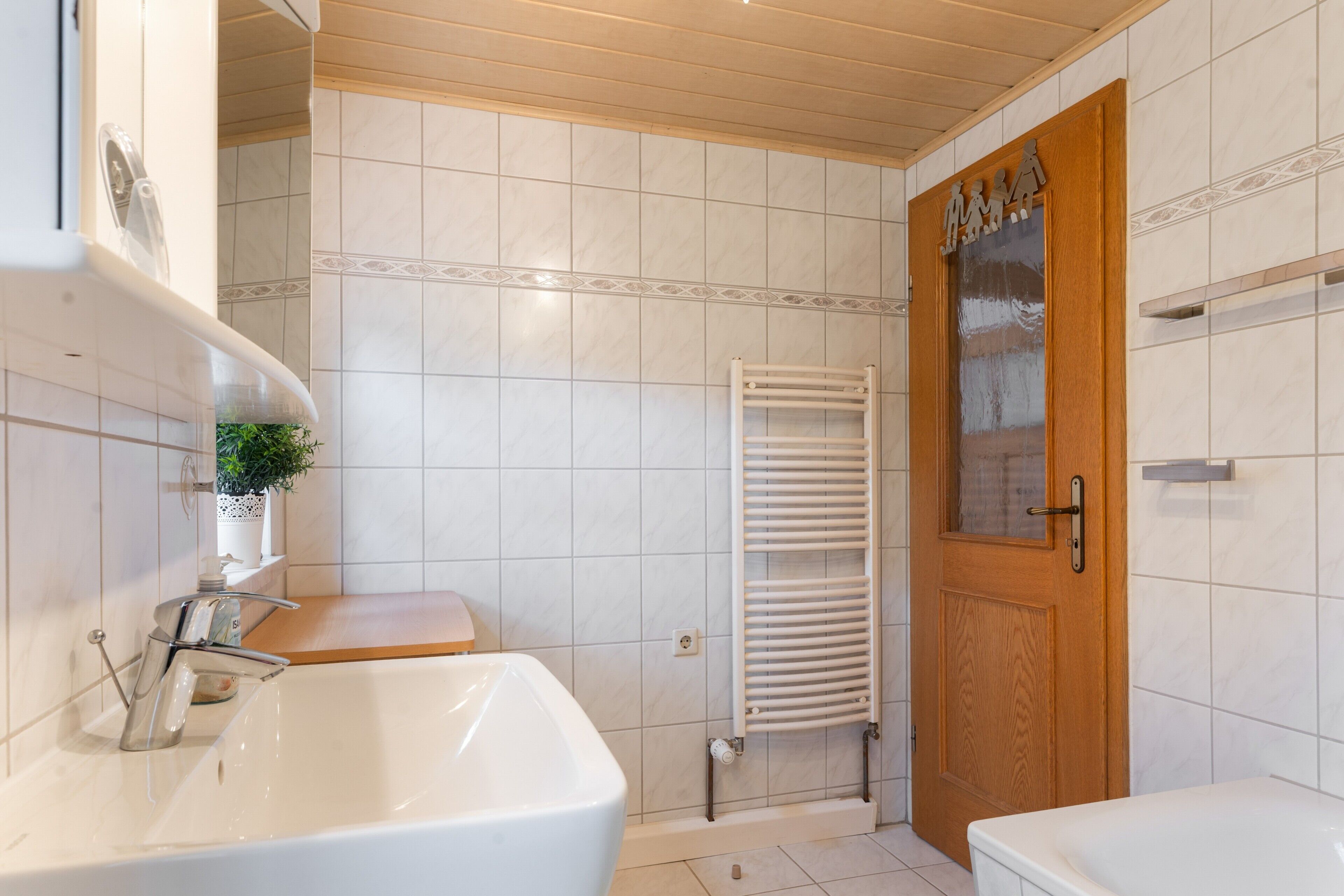 Un baño con un lavamanos blanco, una puerta de madera y un perchero para toallas.