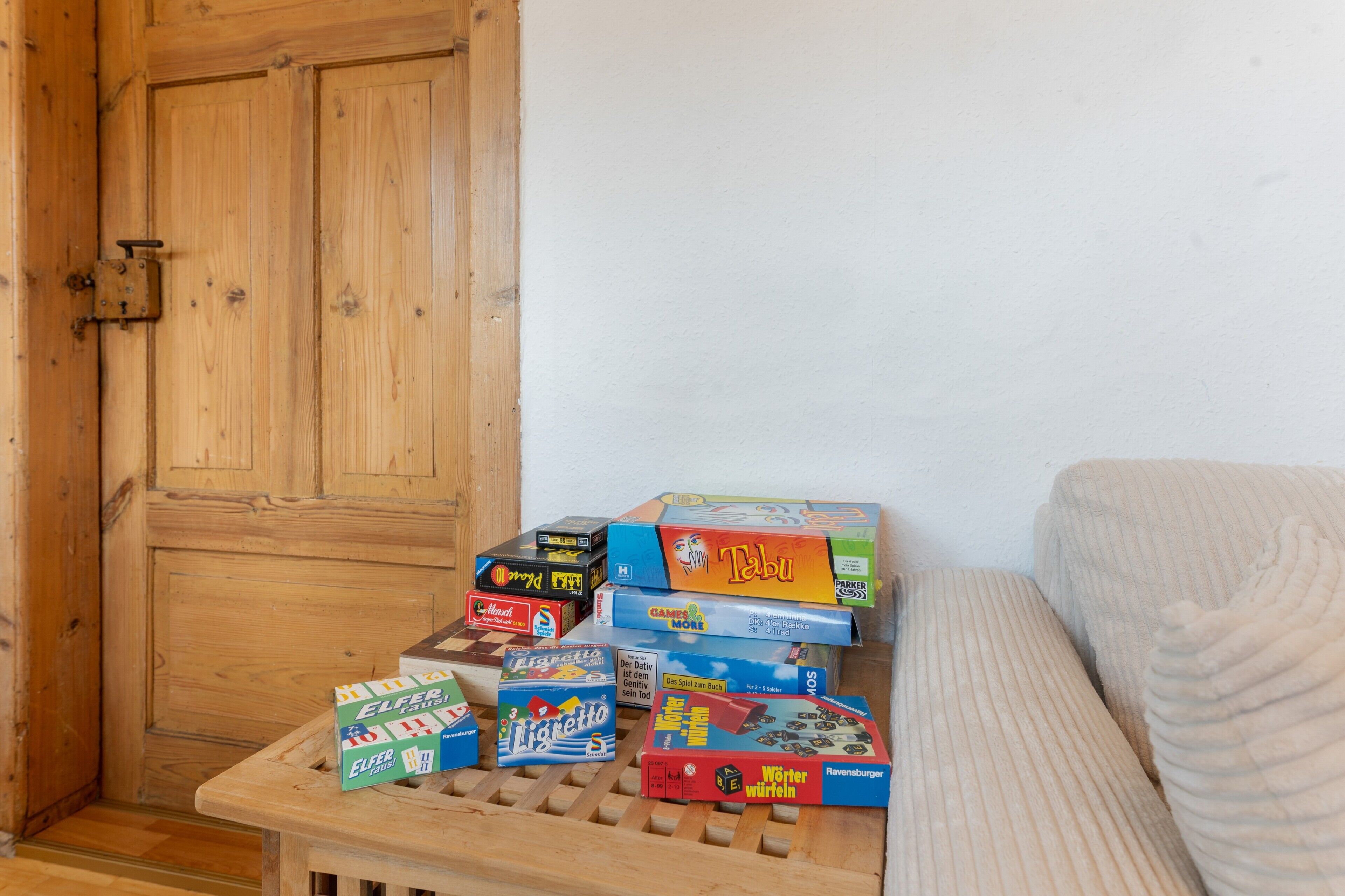 Verschiedene Gesellschaftsspiele auf einem kleinen Holztisch in einem Raum mit Holztür und weißer Wand.