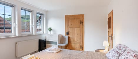 A bedroom with a bed, a chair, a radiator, a wooden door, and a window with a view of buildings.