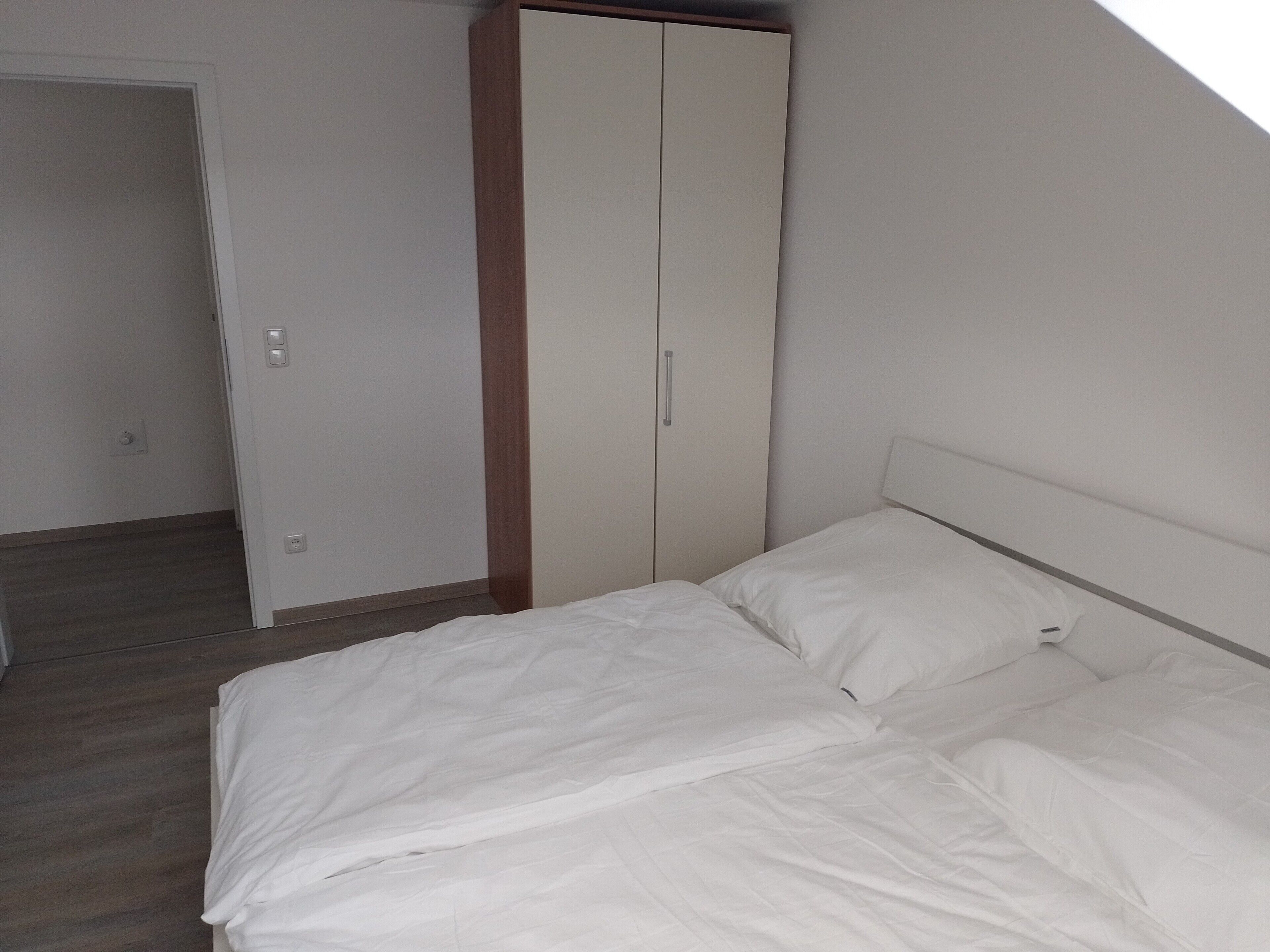 Ein Schlafzimmer mit einem Bett, einem Kleiderschrank und einer Tür zu einem weiteren Raum.