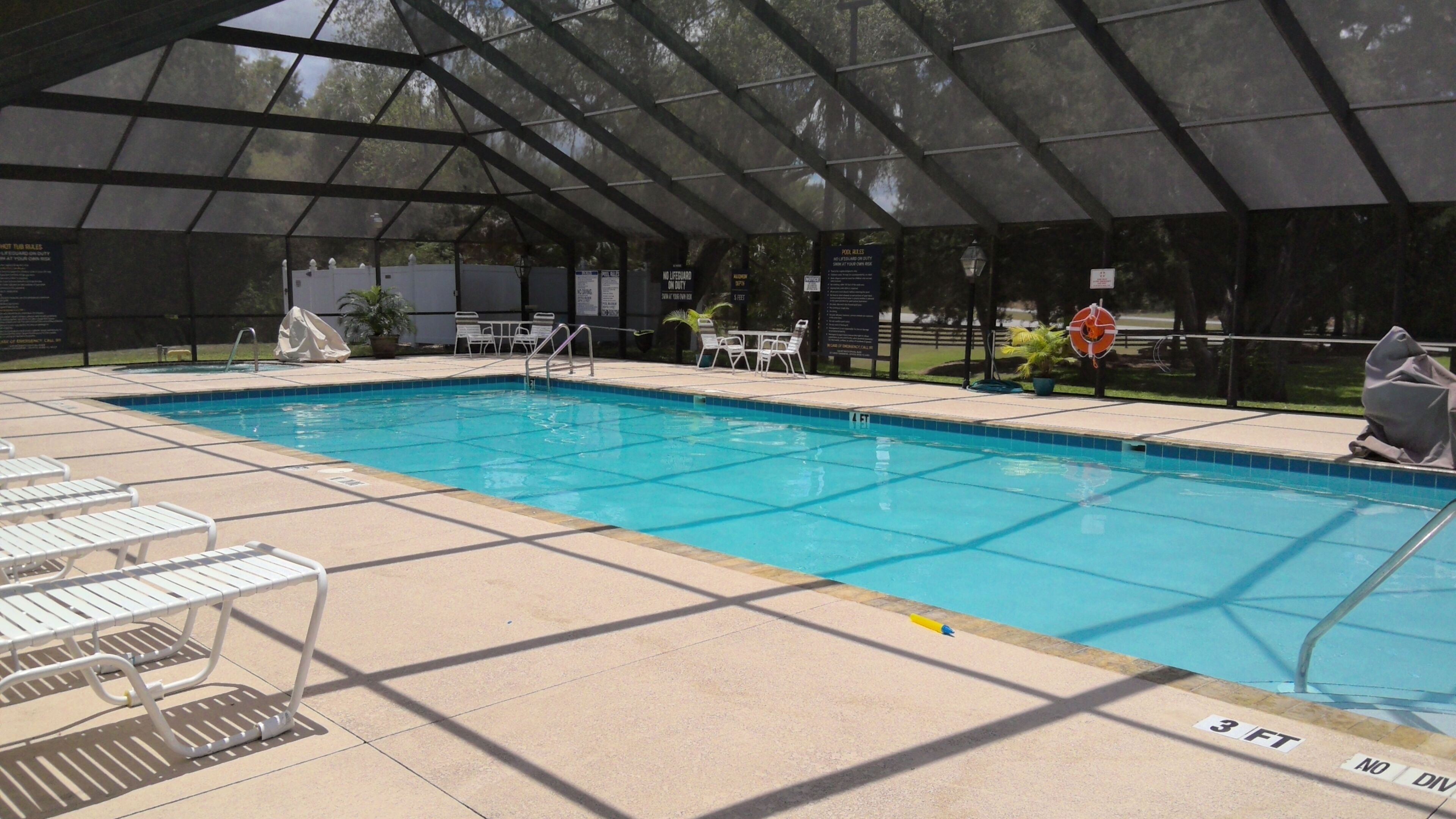 Piscina interior con agua cristalina, rodeada por un área techada con asientos y señales de seguridad.