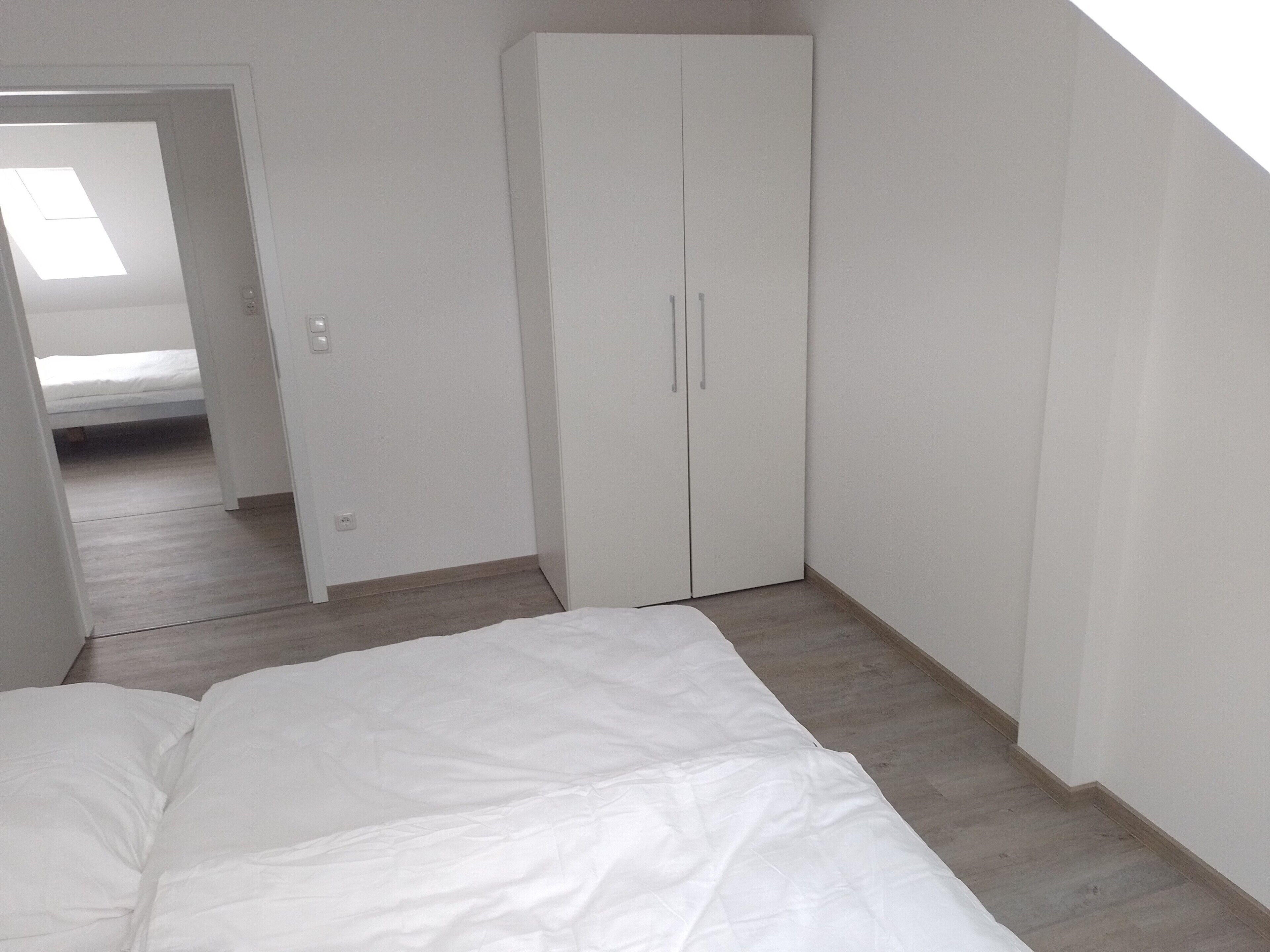 A bedroom with a bed, a wardrobe, and a door leading to another room.