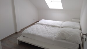 A bedroom with a sloped ceiling, a skylight, a bed with white bedding, and a wooden floor.