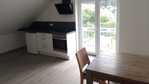 A kitchen with a stove, oven, and black countertop. There is a dining table with a chair.