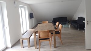 A spacious room with a wooden dining table and chairs, a black sofa, and a glass coffee table.