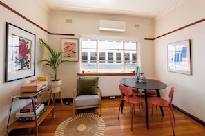 A room with a window, a table with chairs, a bookshelf, and a potted plant. - Charming Art Deco Unit in East Melbourne (East Melbourne)